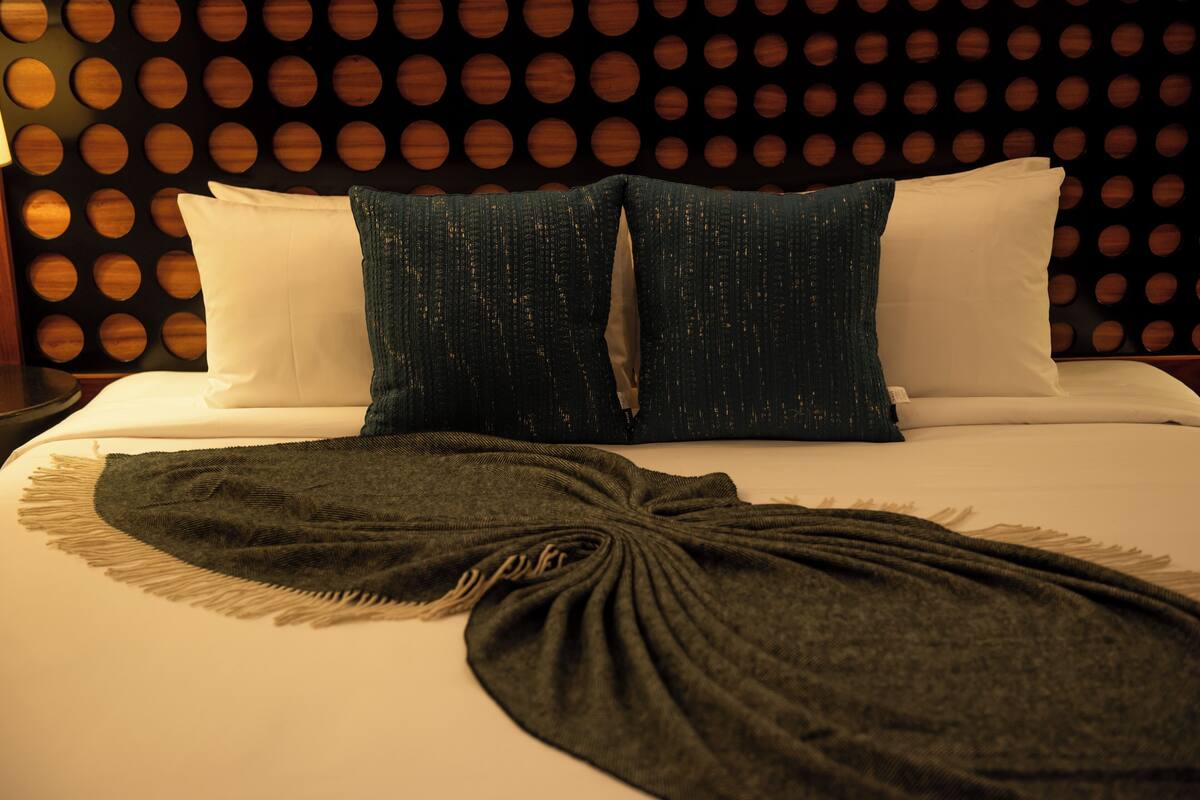 Un lit avec des oreillers blancs et bleu foncé, un plaid vert foncé et un mur orné de motifs circulaires.