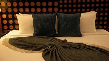 Ein Bett mit weißen und dunkelblauen Kissen, einer dunkelgrünen Tagesdecke und einer Wand mit kreisförmigen Mustern.