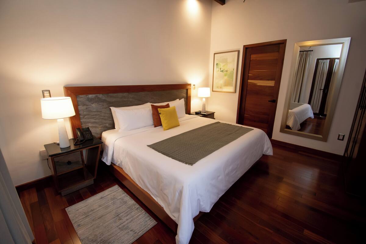 Une chambre d’hôtel bien aménagée, avec un grand lit, des lampes de chevet, une table de nuit, un miroir et un plancher en bois.