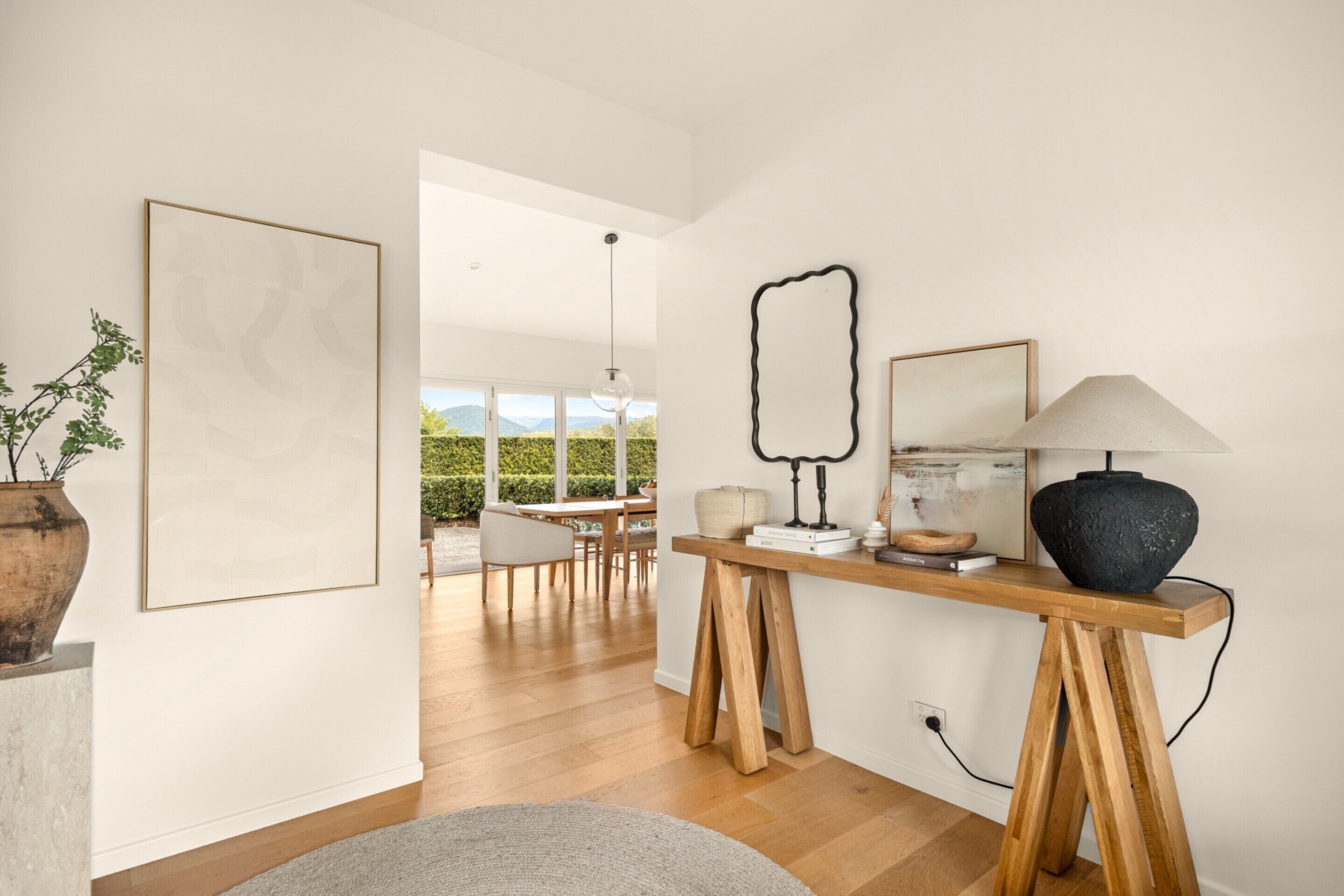 Un intérieur moderne avec un plancher en bois, un tapis rond, une table en bois avec une lampe et des œuvres d’art encadrées.