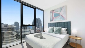 Une chambre d’hôtel moderne dotée d’un grand lit, offrant une vue sur la ville, et agrémentée d’une œuvre d’art contemporaine au-dessus du lit.