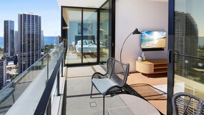 Un balcon doté d’une rambarde en verre, d’une chaise, d’une petite table et d’un téléviseur fixé au mur.