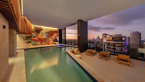 Un espace piscine aménagé sur le toit, offrant une vue sur la ville, avec des chaises longues et une fresque murale.