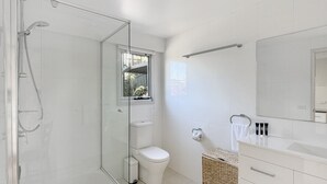 A modern bathroom with a glass shower enclosure, a toilet, a sink with a mirror, and a small window. - Spacious Beach Studio With Alfresco Dining (Surf Beach)
