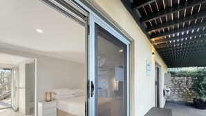 A bedroom with a sliding glass door, a bed, a nightstand, and a small table. - Spacious Beach Studio With Alfresco Dining (Surf Beach)