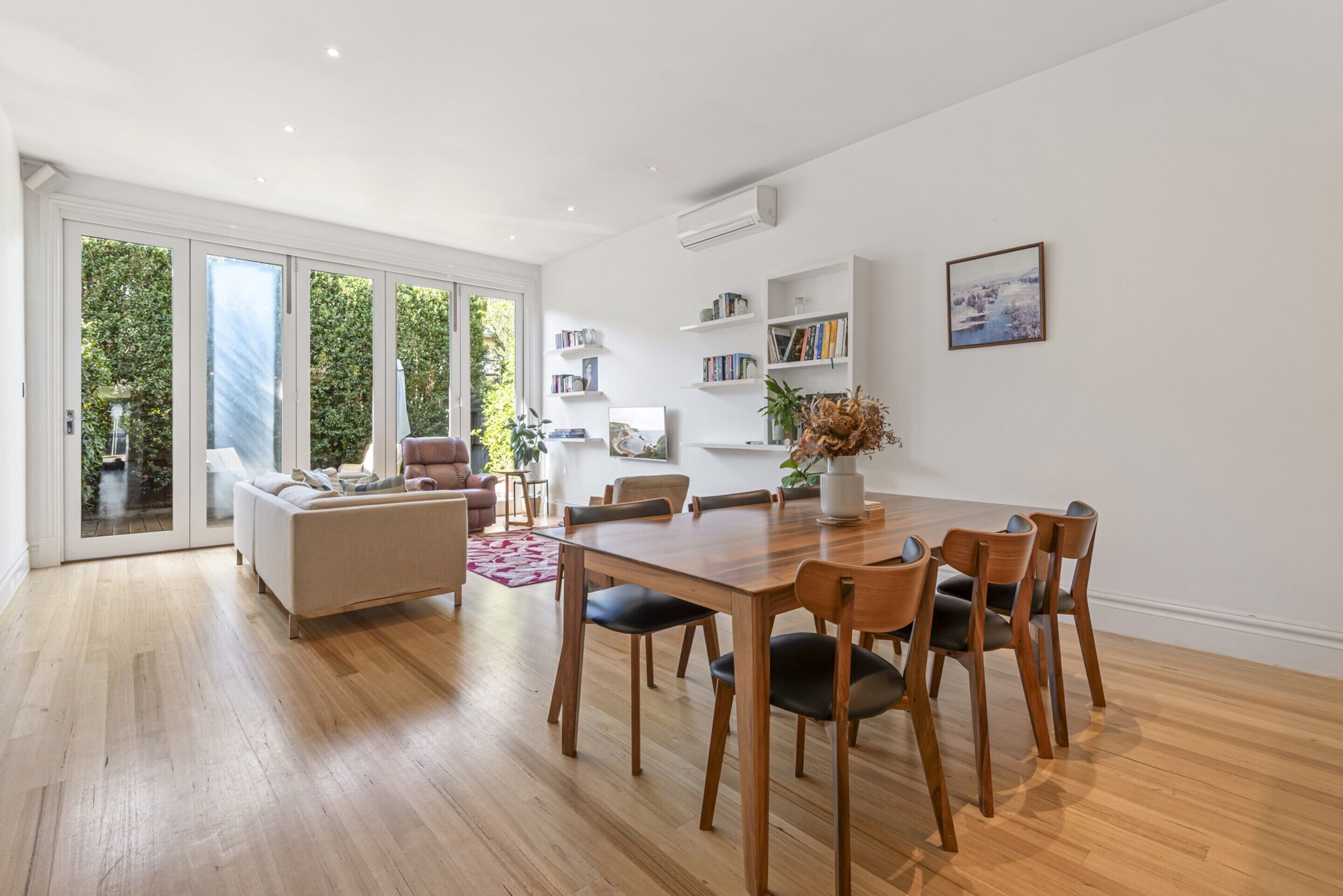 A spacious living area with a wooden dining table, comfortable seating, and a large sliding glass door leading to a garden.