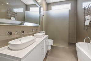 Egy modern fürőszoba, két mosdókagylóval, egy WC-vel és egy fürdőkáddal.