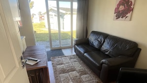 Una sala de estar con un sofá de cuero negro, una mesa de centro de madera y una alfombra gris.
