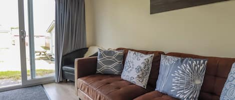 A living room with a brown leather sofa, patterned cushions, a sliding glass door, and a view of the outside.