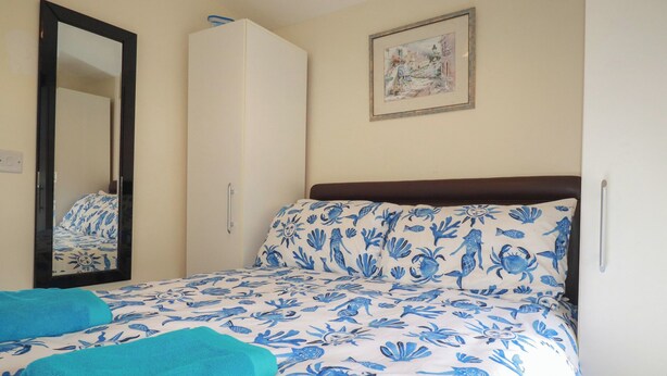 A bedroom with a bed, a wardrobe, a mirror, and a picture on the wall. - Stanbury (Padstow)