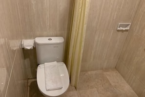 A bathroom with a toilet, a towel, and a toilet paper holder. - Hotel Daily Inn (Central Jakarta)