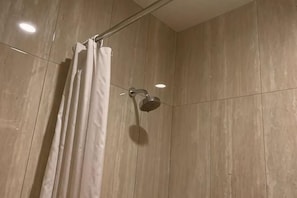 A shower with a curtain, a handheld showerhead, and a wall with a wooden texture. - Hotel Daily Inn (Central Jakarta)