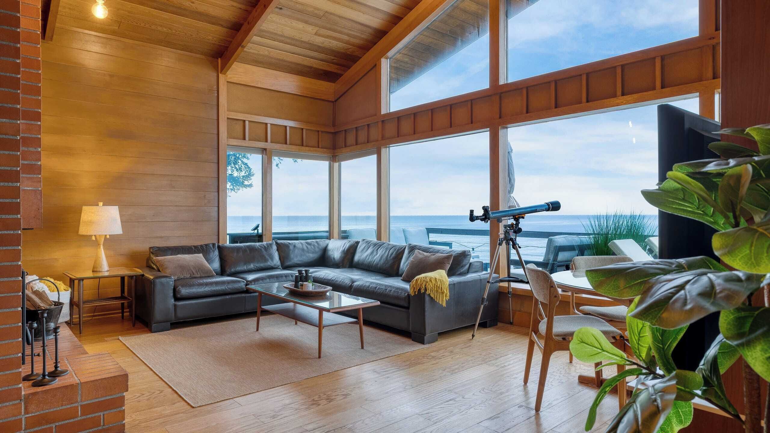 Un salon moderne doté d’une grande fenêtre donnant sur la mer, d’un canapé en cuir, d’une table basse et d’un télescope.