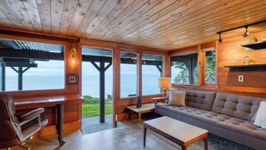 A cozy cabin with a wooden interior, a sofa, a coffee table, and a bar area with a view of the ocean. - Oceanfront Home w/ Outdoor Dining, 2 Firepits + Steps to Beach Salish Sea Escape by Avantstay (Oak Harbor)