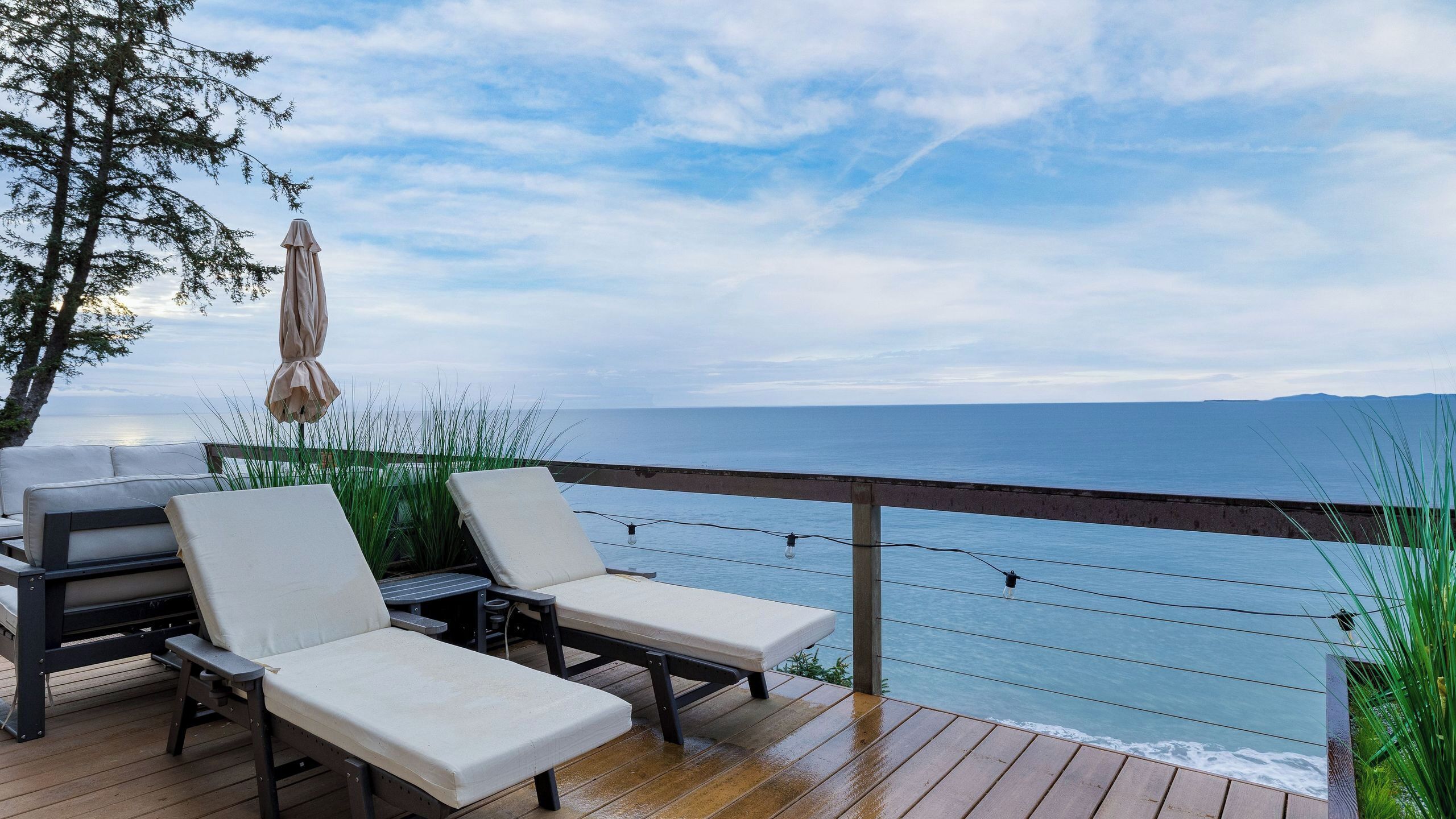 A deck with lounge chairs and a table, overlooking a body of water.