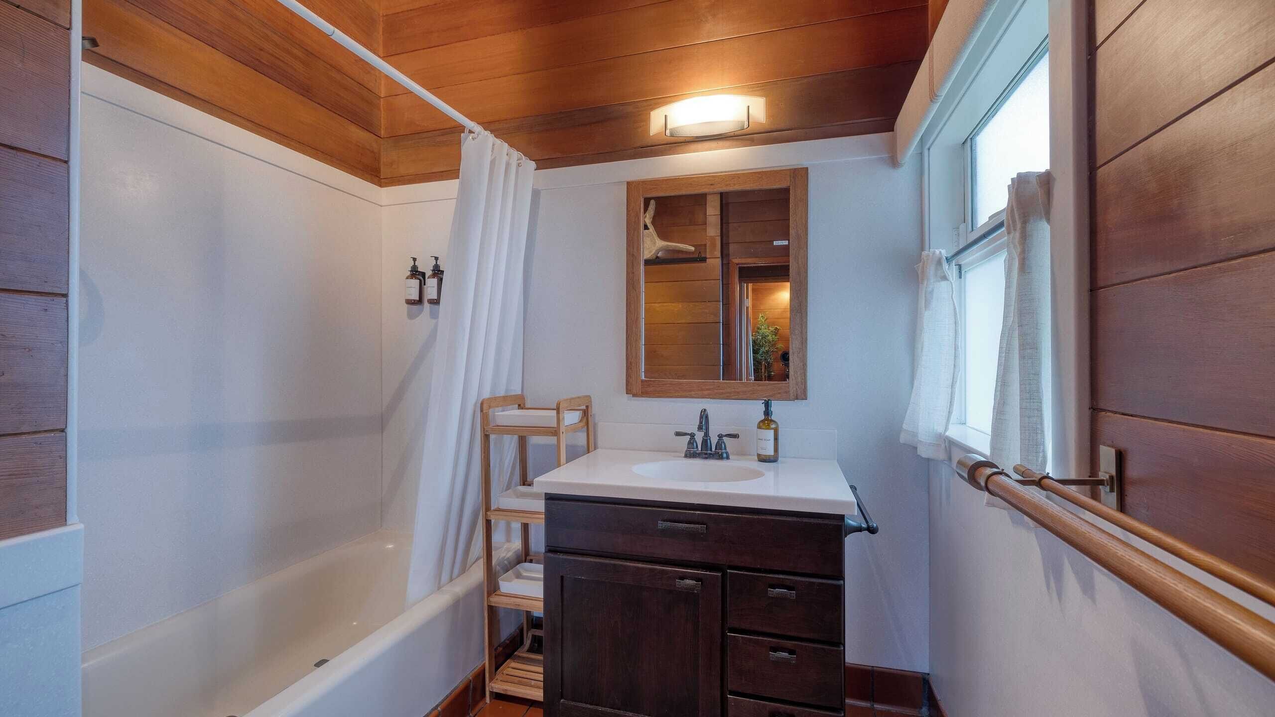 Une salle de bain avec une baignoire, un lavabo avec un miroir, des meubles en bois et une fenêtre.