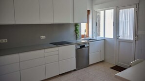 Una cocina moderna con armarios blancos, lavavajillas y una ventana con cortinas.
