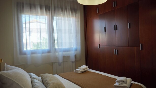 Una habitación de hotel con cama, armario grande y ventana con cortinas traslúcidas.