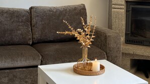 Una sala de estar con una mesa de centro blanca, un sofá marrón, una chimenea y adornos en un estante.
