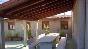 Un patio al aire libre con bancos y mesas de piedra, rodeado de plantas en macetas y muros de piedra.