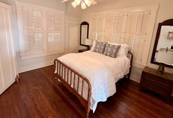 A bedroom with a wooden bed, white shutters, a nightstand, and a mirror. - Beautiful Historic Home in Monte Vista (San Antonio)