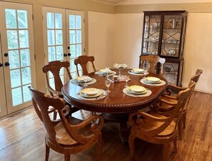 A dining room with a round wooden table set for six, surrounded by six wooden chairs.