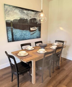 A dining table with six chairs, a large painting above it, and a hanging light fixture. - New Waterfront Home: Enjoy Lake LBJ Water Views From Every Bedroom | Luxury (Granite Shoals)