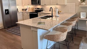 Cozinha moderna com armários brancos, geladeira de aço inoxidável, micro-ondas e uma ilha grande com banquetas.