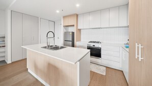 Eine moderne Küche mit weißen Schränken, einer zentralen Kochinsel mit Spüle, einem eingebauten Backofen und einem Edelstahl-Kühlschrank.