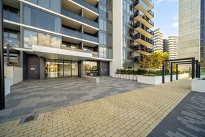 A modern apartment building with multiple balconies, a covered entrance, and a landscaped courtyard. - Stylish 2-bed Apartment With Luxe Amenities Access (Canberra)