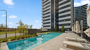 Ein moderner Poolbereich mit Liegestühlen und einem Hochhaus im Hintergrund.