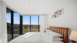 Ein Hotelzimmer mit einem großen Bett, einem Nachttisch, einer Lampe und Blick ins Freie.