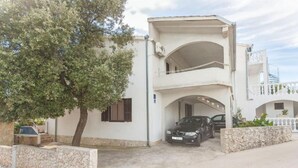 Un bâtiment à deux étages avec une voiture garée dans l’allée, un arbre devant et un mur en pierre.