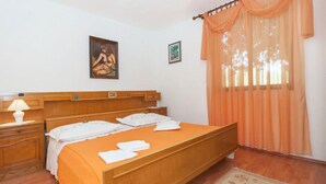 Une chambre à coucher avec un lit en bois, une table de chevet avec une lampe, un tapis à motifs floraux et une fenêtre avec des rideaux orange.