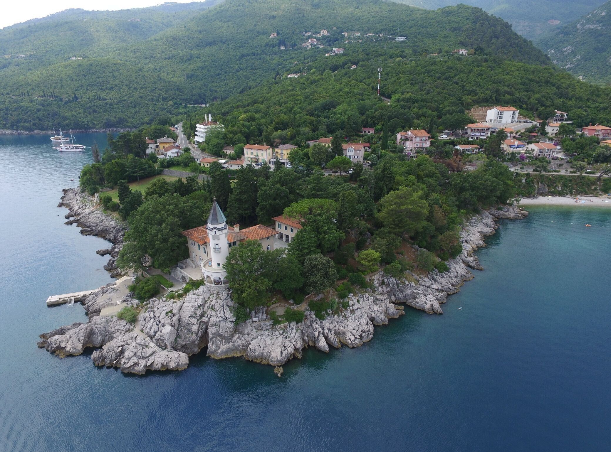 A coastal village with a prominent church on a rocky peninsula, surrounded by lush greenery and residential buildings.