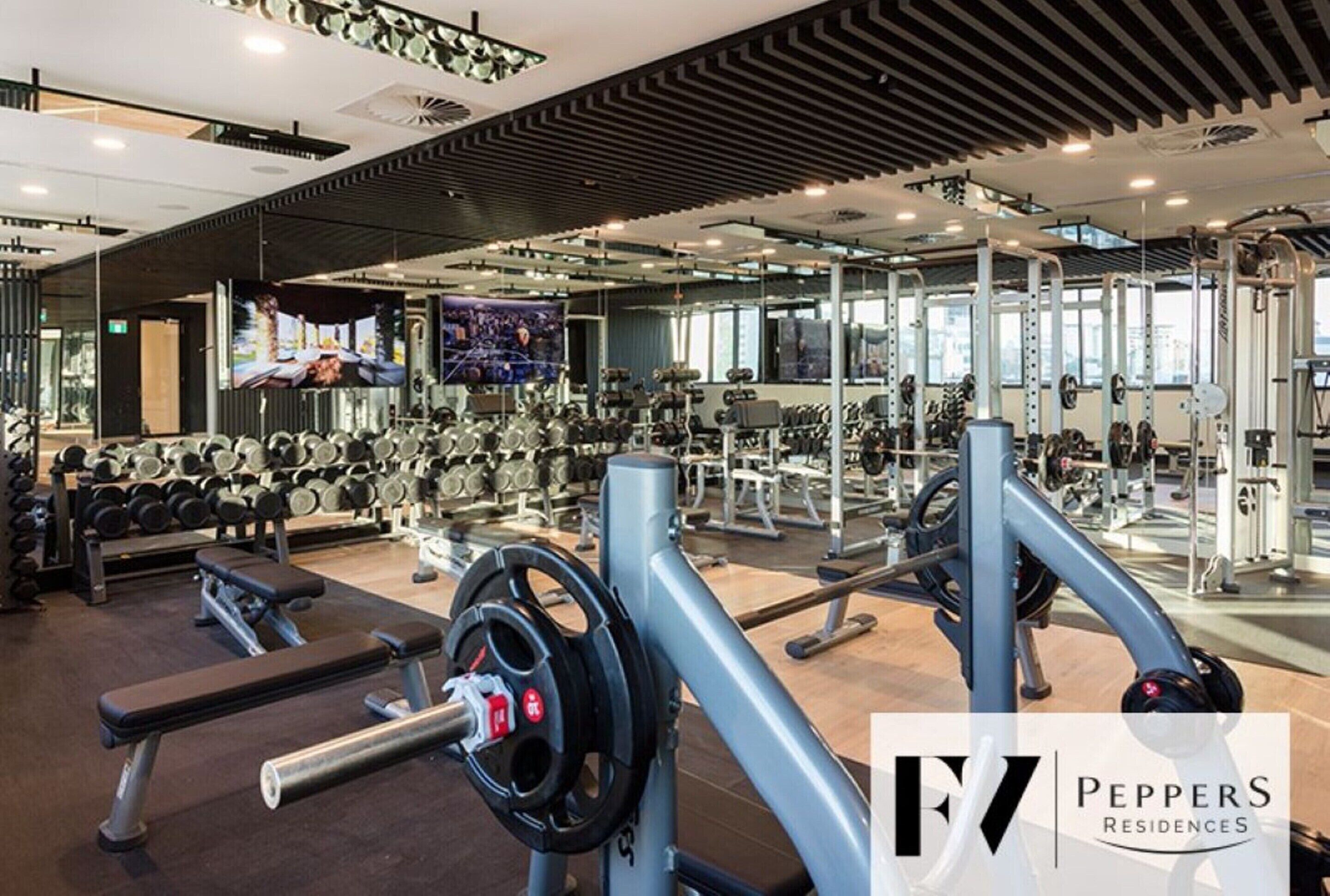 Een sportschool met diverse fitnessapparaten, spiegels en een televisiescherm.