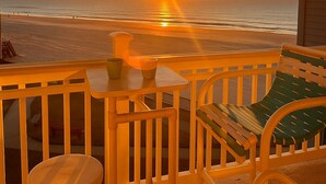 Un balcón con vistas a la puesta de sol sobre el océano, una mesita y una silla.