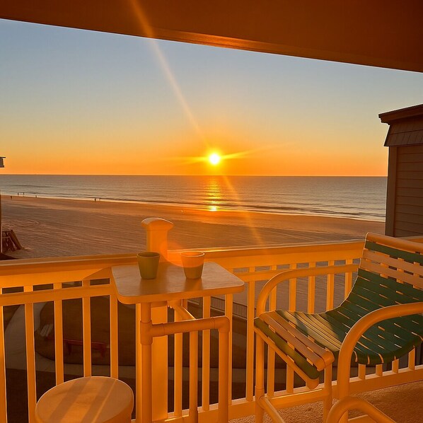 Ein Balkon mit Blick auf den Sonnenuntergang über dem Meer, ein kleiner Tisch und ein Stuhl.