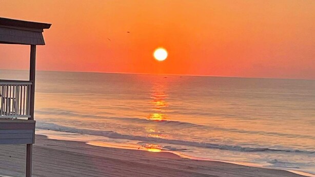 Una playa con una estructura de madera, probablemente una torre de salvavidas, con vista al océano al atardecer.