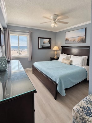 A bedroom with a bed, a nightstand, a lamp, a ceiling fan, and a window with curtains.