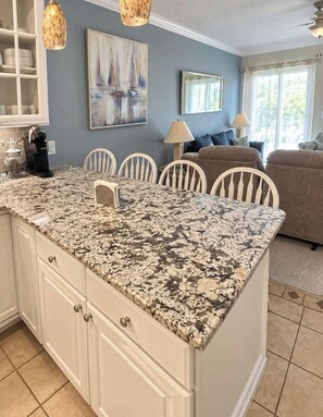 A kitchen with a granite countertop, white cabinetry, and a dining area with chairs.