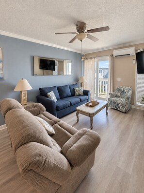 Ein Wohnzimmer mit einem blauen Sofa, beigen Sesseln, einem Holztisch und einem Deckenventilator.