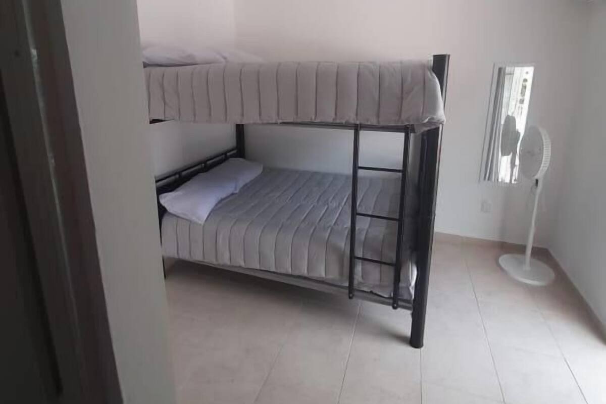 A bunk bed room with a standing fan and a window.