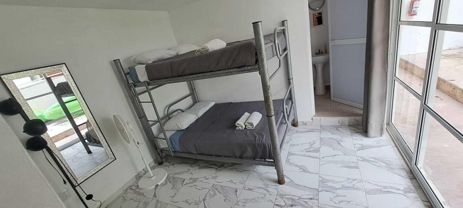 Un letto a castello con uno specchio, una ventola e un bagno sullo sfondo.