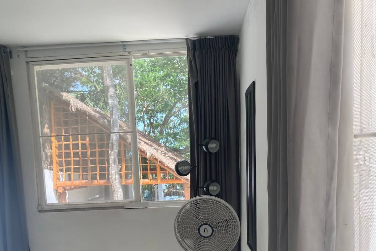 A room with a large window, a standing fan, and a curtain.