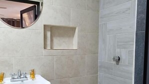 A bathroom with a white pedestal sink, a round mirror, and a small shelf above the sink. - HOTEL SOL (Guadalajara)