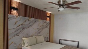 A bedroom with a bed, a ceiling fan, a bedside table, and a wall with a marble-like pattern. - HOTEL SOL (Guadalajara)