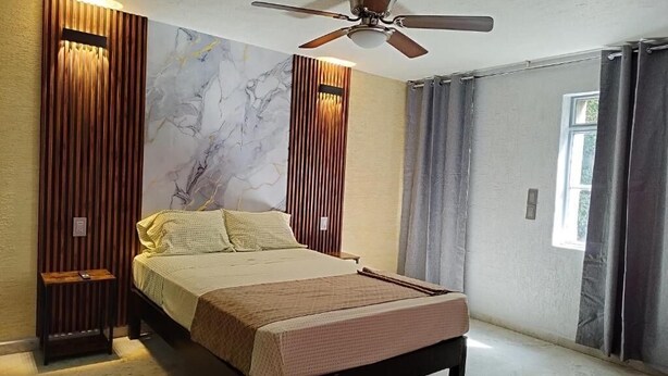 A bedroom with a bed, a ceiling fan, a wall with vertical wooden slats, and a window with curtains. - HOTEL SOL (Guadalajara)