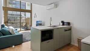 Eine moderne Küche mit integriertem Mikrowellenherd, Geschirrsp üler und Spüle. Im angrenzenden Wohnbereich befindet sich ein graues Sofa mit Kissen.