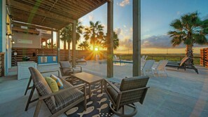 A covered outdoor area with seating, a pool, and a view of the sunset. - Bayfront Home w/ Pool, Game Room + Walk to Beach & Golf Cart Access Pelicans Perch by Avantstay (Port Aransas)